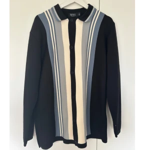 Randig kofta från boohooMAN i blått och svart - Snygg kofta från boohooMAN med vertikala ränder i blått, svart och beige. Tröjan har knappar hela vägen och en klassisk krage. Materialet är stickat och känns mjukt mot huden. Perfekt för dig som gillar retrovibbar och vill sticka ut med coola färgkombinationer.