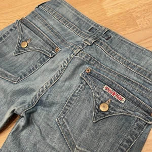 Låga Vintage Hudson bootcut jeans med knappar - Snygga blå jeans från Hudson med bootcut passform och låg midja. Min mammas gamla från 2000- talet, byxorna är insydda i midjan samt uppsydda några centimeter, därför stämmer inte storlek på lappen med verkligheten. På lappen står det strl 29, skulle uppskatta det som en 27 nu. Små fläckar som inte går bort i tvätten samt slitage mellan låren, se sista bilden. Mått: Midja - 34cm, Höfter - 44cm, Innerben - 78cm(+4), Ytterben - 97cm(+4), Midjehöjd - 20cm 