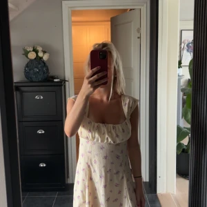 Ljus blommig sommarklänning - Säljer en söt ljus klänning med små lila blommor och romantisk skärning. Klänningen har korta ärmar och en mjuk, feminin form med lätt rynk vid bysten. Perfekt för varma dagar och har en fräsch, somrig vibe.