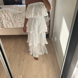 Vit långklänning med volanger - Superfin vit långklänning med flera lager volanger och elastisk midja. Klänningen kan bäras både offshoulder och med axelband, vilket ger en flexibel look.