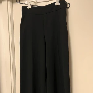 Svarta wide kostymbyxor från H&M - Snygga svarta kostymbyxor från H&M i storlek 32. Byxorna har en hög midja och ett wide ben som ger en trendig och chill siluett. Perfekta att matcha med en crop top eller hoodie för en cool look. Materialet känns mjukt och har ett fint fall.