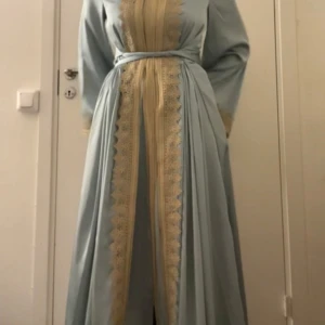 Ljusblå långklänning med spetsdetaljer  - Säljer en elegant ljusblå långklänning med breda ärmar och vackra spetsdetaljer i beige längs mittpartiet och vid ärmsluten. Klänningen har ett matchande bälte i midjan som knyts för en snygg siluett. Perfekt för dig som gillar klassisk och sofistikerad stil. .den är endast provad. Och hans gjord i maracco 