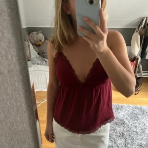 Vinröd topp från Nelly - Supersöt vinröd linnetopp från Nelly med tunna axelband och v-ringning. Toppen har spetsdetaljer längs ringningen och nederkanten samt en liten rosett framtill. Använd en gång så är som ny💓