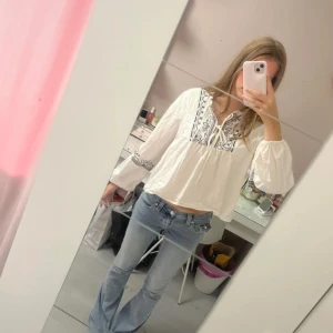 Vit broderad blus från ONLY - Supersöt vit blus från ONLY med svarta broderier på ärmar och vid halsringningen. Blusen har knytband framtill, v-ringning och vida långa ärmar.