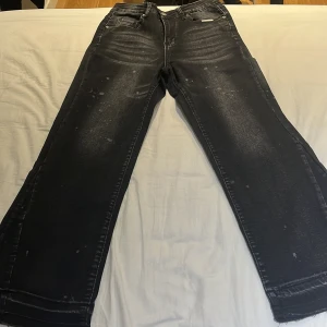 Svarta flared jeans från Gurbaks - Svarta flared jeans från Gurbaks som inte passade mig med breda ben och coolt slitna detaljer. Byxorna har klassisk femficksdesign, metallmärke vid fickan och läderpatch med 'Fashion Jeans' bak. Materialet är jeans och färgen är mörk med blekta partier för en edgy vibe. Storlek: XS 