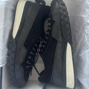 Svarta sneakers från Dsquared2 - Säljer ett par svarta sneakers från Dsquared2 med coolt mönstrade snören och robust sula med rutmönster. Skorna har detaljer i både mocka och skinn, samt en vit kontrast på mellansulan. Perfekt för dig som gillar stilrena och sportiga vibes.