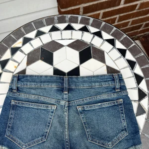 Blå jeansshorts med fransad kant - Snygga blå jeansshorts med fransad kant och klassisk femficksdesign. Shortsen har låg midja, slitna detaljer och en cool tvätt som ger en avslappnad vibe. Perfekta för sommaren och passar till allt från t-shirt till blus.