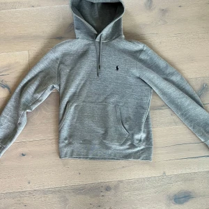 Grå hoodie från Polo Ralph Lauren - Hej! Säljer en stilren grå hoodie från Polo Ralph Lauren med klassisk huva och snörning. Tröjan har en broderad svart logga på bröstet och en stor magficka. Perfekt för chill dagar och enkel att matcha med jeans. Köpt i butik i Stockholm. Andvänd varsamt men mycket. Hör av dig vid minsta fundering! Mvh Leo. Ps pris ej hugget i sten.
