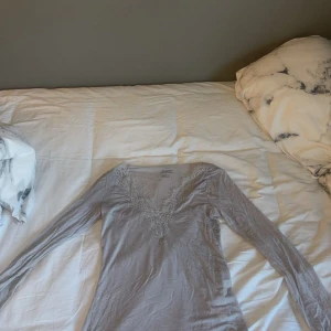 Grå v-ringad tröja med spets Intimissimi - Supersnygg grå långärmad tröja från Intimissimi med v-ringning och fina spetsdetaljer runt halsen. Mjuk och tunn kvalitet med inslag av kashmir, perfekt för dig som gillar stilrena och feminina plagg. Sitter snyggt och är lätt att matcha med jeans eller kjol.