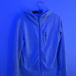 Sail racing tröja - Vit hoodiejacka från Sail Racing med dragkedja framtill och en extra ficka med zip på bröstet. Jackan har huva med snörning och lång ärm, perfekt för chill dagar. Snygg logga på bröstet och sportig look.
