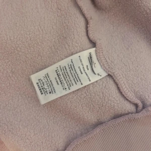 Ljusrosa fleecejacka Peak Performance - Mysig ljusrosa fleecejacka från Peak Performance med huva och hel dragkedja i rosa. Jackan har två stora fickor framtill och broderad logga på bröstet. Perfekt för chill dagar och när du vill hålla dig varm. Snygg och enkel design som funkar till allt.