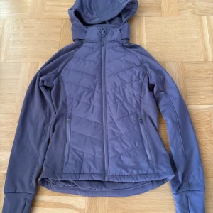 Lila pufferjacka från H&M Move - Snygg lila pufferjacka/hoodie från H&M Move med huva och hel dragkedja framtill. Jackan har två sidofickor med dragkedja och quiltade detaljer på framsidan. Perfekt för dig som vill ha en sportig och stilren look under kyliga dagar.