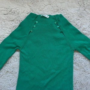 Grön stickad tröja med knappar från mango - Snygg grön stickad tröja från MNG i storlek M. Tröjan har rund hals och dekorativa knappar längs axlarna. Långärmad och mjuk i materialet, perfekt för dig som gillar enkel men cool stil. Passar dig som vill ha något färgglatt och bekvämt. Inga defekter förutom en liten tråd dragning i höger arm, jätte bra skick! Jag med storlek xs kan ha tröjan så den passar både xs-M