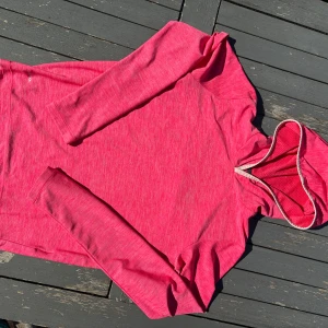 Rosa hoodie från Helly Hansen - Snygg rosa hoodie från Helly Hansen med diskret logga på bröstet. Tröjan har långärmade ärmar och huva med meshfoder. Materialet är mjukt och lätt polyester, perfekt för träning eller chill. Tumhål i ärmsluten för extra komfort. Passar dig som gillar sportig stil.