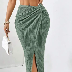 Grön omlott långkjol med slits/sett - Snygg grön långkjol med omlott-design och slits framtill. Kjolen har en ribbad struktur som ger cool textur och sitter tight över höfterna. Perfekt för dig som gillar trendiga och stilrena plagg med lite edge.