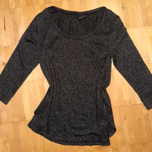 Mörkgrå trekvartärmad topp - Säljer en jättefin stilren mörkgrå trekvartsärmad topp med rund halsringning. Toppen har en figurnära passform och är tillverkad i ett mjukt, stretchigt material. Den passar till allt och säljs inte längre!