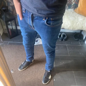 Blå slim jeans från Nudie Jeans - Säljer ett par blå skinny jeans från Nudie Jeans i modellen Thinn Finn(slim). Klassisk femficksdesign, snygga kontrastsömmar och ikonisk våg på bakfickan. Jeansen är i stretchig denim som sitter tajt hela vägen ner. Priset är inte huggg i sten!