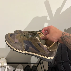 Valentino Rockrunner sneakers camouflage - Säljer ett par Valentino Rockrunner sneakers med grön och brun camouflage, detaljer i mocka och skinn samt coola nitar runt sulan, skorna är äkta men har tyvärr ingen låda. Lite slitage därav priset