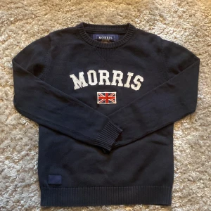 Stickad Morris crewneck  - Säljer en stilren marinblå stickad Morris crewneck. Den är i fint skick 9/10, texten på lappen bild 4 har gått bort men annars inga defekter. Skriv gärna över frågor och funderingar, priset kan diskuteras.