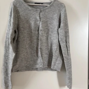 Grå kofta med knappar - Säljer en stilren grå kofta med rund hals och knäppning framtill. Perfekt för lager på lager under kyligare dagar. Koftan har långa ärmar och en mjuk känsla. Fint till sommaren med ett linne under och en knapp stängd bara❤️ Använd få tal gånger❤️