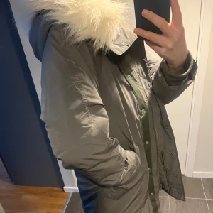 Filippa K dunjacka - Grön-grå dunjacka från Filippa K. Har en liten defekt på ärmen i form av brännmärke annars mycket gott skick.