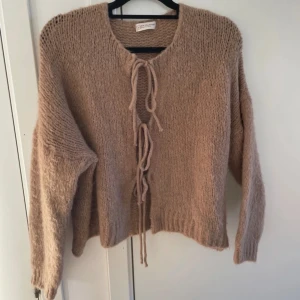 Beige stickad kofta från New Collection - Mysig beige stickad kofta från New Collection, tillverkad i Italien. Koftan har långa ärmar och knytband framtill för en avslappnad look. Perfekt för kyliga dagar.