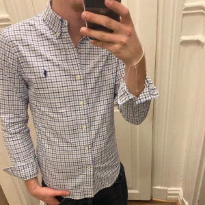 Rutig skjorta från Ralph Lauren - Snygg rutig skjorta från Ralph Lauren i blått och vitt. Skjortan har en slim fit passform. Den har långa ärmar och knappar framtill. Modellen är ca 182, tveka inte att kontakta vid eventuella frågor 😀