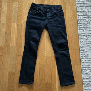mörka blåa från Nudie Jeans - Snygga mörkblåa jeans från Nudie Jeans med klassisk femficksdesign och knappgylf. Jeansen har en rak passform och är perfekta clean look. De har en liten fläck på högra bakficka, men inget som märks. Storlek W31, L32.