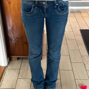 Blå jeans från LTB - Snygga blå jeans från LTB med klassisk femficksdesign och knappgylf. De har en bekväm passform och är perfekta för en avslappnad stil. Märkeslogga på baksidan av midjan. Storlek 26/32. Midjemått rakt över 36 cm. Innerbenslängd 79 cm. 