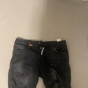 Svarta jeans med färgstänk - Snygga svarta jeans från Dsquared2 med unika färgstänk och slitningar. De har en knappgylf och klassisk. Shorts.femficksdesign. Perfekta för en trendig och avslappnad stil.