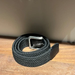 Svart flätat bälte från Jack&Jones - Snyggt svart flätat bälte med en stilren silverfärgad spänne. Perfekt för att ge en extra touch till din outfit. Bältet har en klassisk design som passar till många olika stilar.Nypris 249kr Och är 95cm långt. Metallen Längst fram har lite repor så därför är priset lågt. 