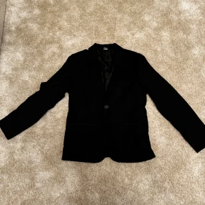 Svart kavaj från Lindex - Snygg svart kavaj från Lindex i storlek 152. Perfekt för festliga tillfällen. Kavajen har en klassisk design med en knapp framtill och är tillverkad i ett stilrent material.  Skick: 9/10 Färg: Svart Storlek: 152 Ord. Pris: 399  Din stil: Missa inte chansen till en elegant kavaj i nyskick. Ställ frågor om du undrar över något. Inte din stil: kanske som en present till någon? Annars kika in mina andra annonser som jag har lagt upp. Finns något för alla åldrar och kön.