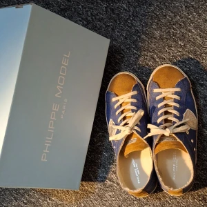 Blå och bruna sneakers från Philippe Model - Snygga sneakers från Philippe Model i en cool kombination av blått och brunt. Skorna har vita snören och en unik design med silverdetaljer på sidan. Perfekta för en avslappnad stil med en touch av elegans. Använda endast 2 gånger. Hör gärna av dig vid funderingar! Priset går att diskutera vid snabb affär! Skriv om du vill ha fler bilder med! 😁 sulan är inte med. Men kommer med ny sula. Kvitto finns! 