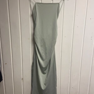 Mintgrön tajt långklänning - Elegant grön långklänning med smala axelband, knytning i ryggen och en slit nedtill.💚