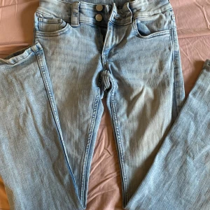 Ljusblå bootcut jeans från H&M - Snygga ljusblå bootcut jeans från H&M med justerbar midja och låg midja. De har två knappar fram och fickor med knappdetaljer bak. Perfekta för en avslappnad stil.