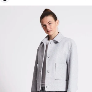 Grå kappa med knappar - Snygg grå kappa med knappar framtill och stora fickor. Perfekt för en stilren look. Jackan har en klassisk krage och är långärmad.