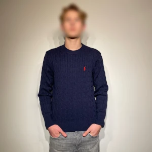 Mörkblå stickad tröja från Ralph Lauren - Säljer en snygg mörkblå stickad tröja från Ralph Lauren med det klassiska röda logotypen på bröstet. Tröjan har en stilren design med kabelstickat mönster och långa ärmar. Perfekt för en stilren look! Storlek: M. Lappen finns kvar, den är aldrig använd utan bara testad för bilder. Priset är diskuterbart. Skriv vid minsta fundering!