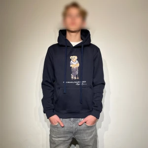 Mörkblå hoodie från Ralph Lauren - Säljer en snygg mörkblå hoodie från Ralph Lauren med det ikoniska Polo Bear trycket på framsidan. Perfekt för en avslappnad stil. Storlek: M. Lappen finns kvar, den är aldrig använd utan bara testad för bilder. Priset är diskuterbart. Skriv vid minsta fundering!