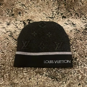 Svart mössa - Snygg svart med diskret mönster och logotyp. Mössan har en grå rand och är perfekt för att hålla värmen med stil.