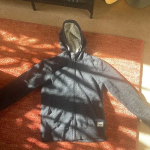 Mörkblå lurvig hoodie från H&M - Säljer en mörkblå hoodie från H&M med dragkedja och huva. Insidan är fodrad med mjukt material för extra värme. Perfekt för kyliga dagar. Bra skick 