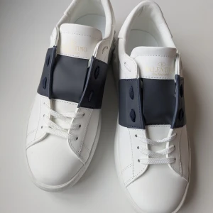 Valentino Garavani sneakers - Snygga vita Valentino Garavani sneakers med mörkblå detaljer. Skorna har en stilren design med snörning och en bekväm sula. Perfekta för en trendig look. Kvitto finns tyvärr inte 