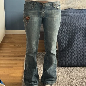 Blå bootcut jeans med blommig brodering - Säljer mina jättesnygga blå bootcut jeans med fin blommiga broderier på sidan. Älskar verkligen dessa jeans på grund av blommorna och passformen, perfekt booutcut men tyvärr har de börjat bli för små i midjan för mig.💙 jag skulle säga att storleken är 34/36 men lättast är att jämföra med sina mått: Midjemått:39/40 rakt över Innerbenslängd: 82 