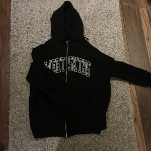 Zip Hoodie Sweet SKTBS  - Säljer en svart Zip hoodie från Sweet SKTBS med dragkedja och broderat tryck på framsidan. Perfekt för en avslappnad stil. Huvan ger extra komfort och värme. Hög kvalité på huvtröjan. Använd Max 5 gånger så näst intill ny. Nypris är 899kr