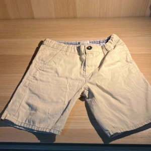 Beige shorts från Lindex - Säljer ett par beige shorts från Lindex. De har en knapp och dragkedja framtill samt fickor på sidorna och en bakficka med knapp. Perfekta för varma dagar.