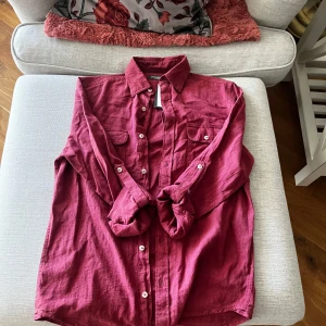 Vinröd linneskjorta från Dressmann - Snygg vinröd skjorta i linneblandning från Dressmann. Skjortan har långa ärmar och knappar framtill samt på bröstfickorna. Perfekt för en stilren look.