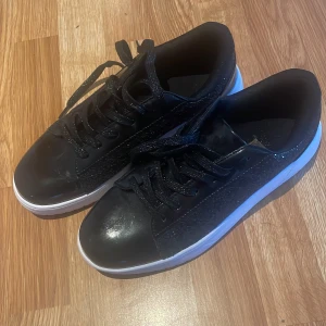 Svarta glittriga sneakers - Snygga svarta sneakers med glittriga detaljer och vit sula. Skorna har snörning och en stilren design som passar perfekt för en trendig look.