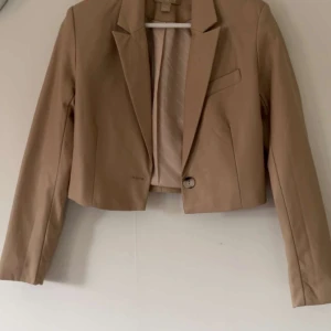 Beige kavaj från Amisu - Snygg beige kavaj från Amisu i en croppad stil. Den har en enkel knapp framtill och långa ärmar. Perfekt för en stilren look.