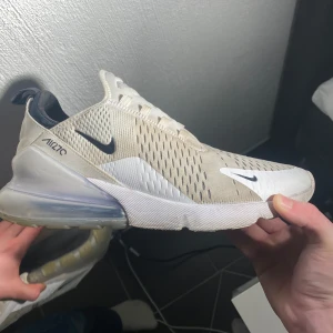 Nike Air Max 270 - Säljer ett par stilrena Nike Air Max 270 med vit och svart detaljering. Skorna har en synlig Air-enhet i hälen och är designade med snörning för en säker passform. Perfekta för en sportig look. Kommer med box