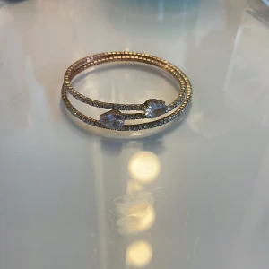 Guldarmband med glittriga detaljer - Elegant guldarmband med dubbla rader och glittriga stenar. Armbandet har två stora, klara stenar i mitten som ger en lyxig känsla. Perfekt för att lyfta vilken outfit som helst.