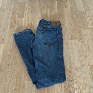 Blå jeans från Lee - Blå jeans från Lee med dragkedja och knapp. De har en rak passform. Storleken är W32 L34.